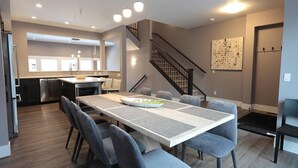 Cozinha moderna com ilha central, área de refeições com mesa comprida e cadeiras, e escada que leva a um andar superior.