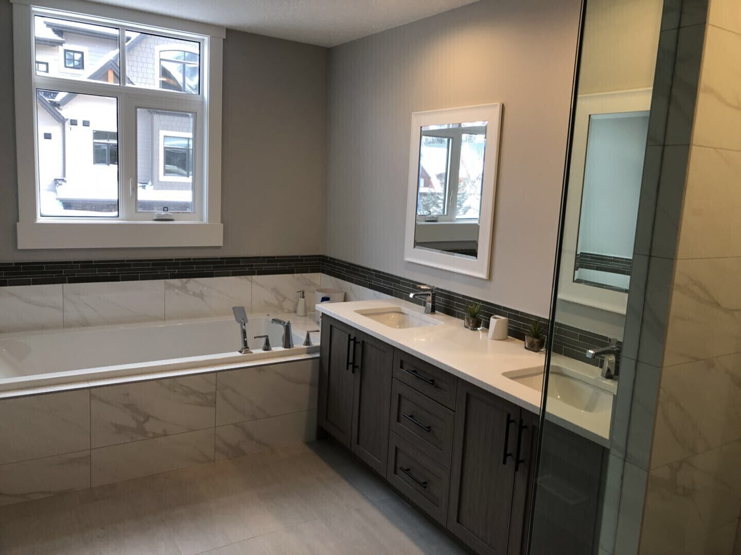 Ein modernes Badezimmer mit einer großzügigen Badewanne, zwei Waschbecken, dunklen Holzschränken und einem großen Spiegel.