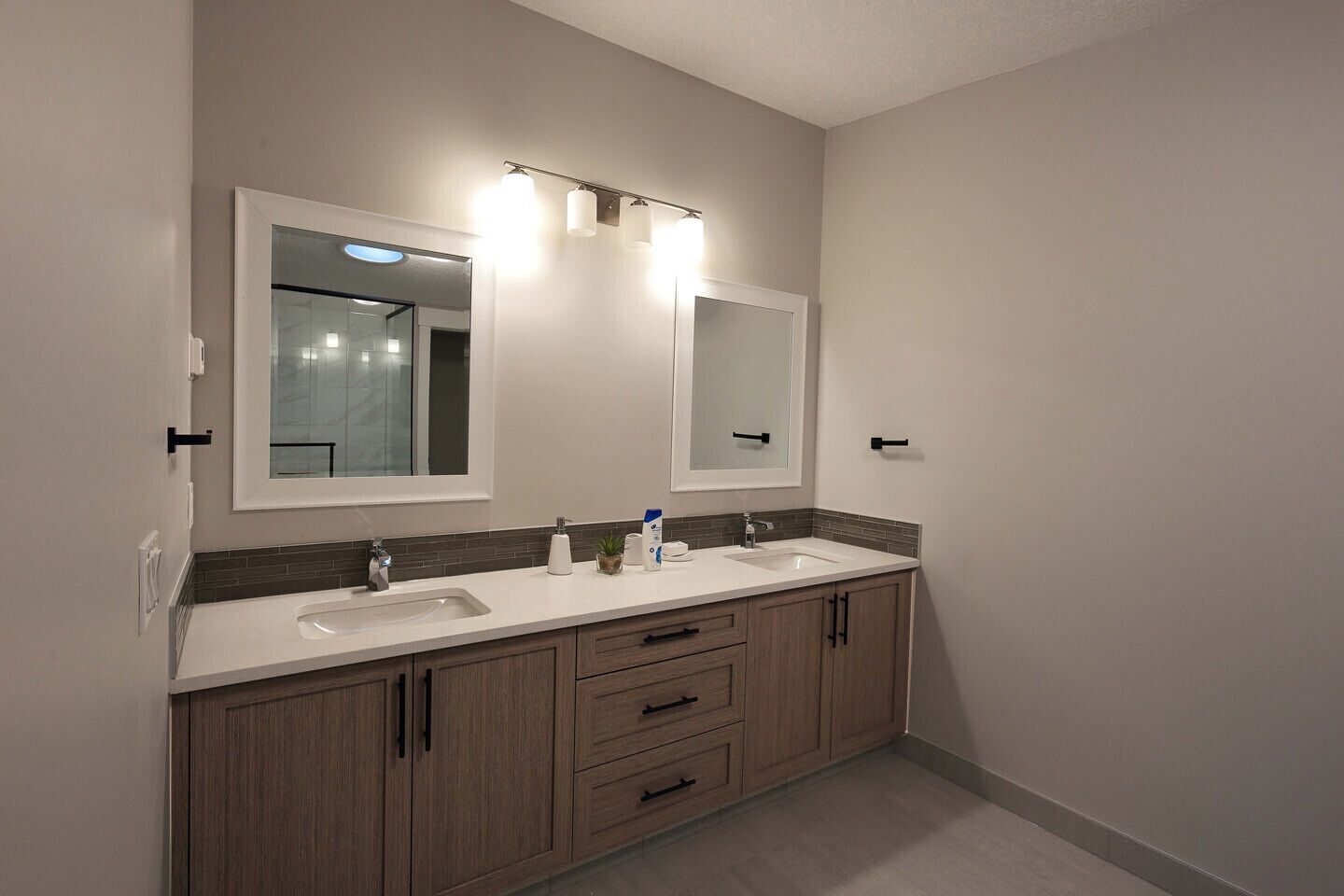 A modern bathroom with two sinks, a large mirror, and a vanity with drawers.
