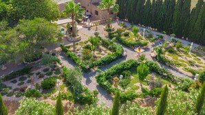 Vista aérea de un jardín con un edificio de piedra, senderos y diversas plantas.