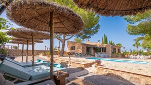 Zona junto a la piscina con sillones, sombrillas y un edificio de piedra al fondo.