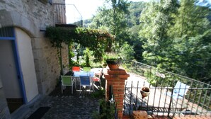 A stone building with a small outdoor seating area, a brick planter, and a metal railing. - Large gîte by the river, private terrace,  (Le Tech)