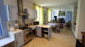 A compact kitchen with a stove, microwave, and built-in oven. There is a dining area with a table and chairs. - Large gîte by the river, private terrace,  (Le Tech)