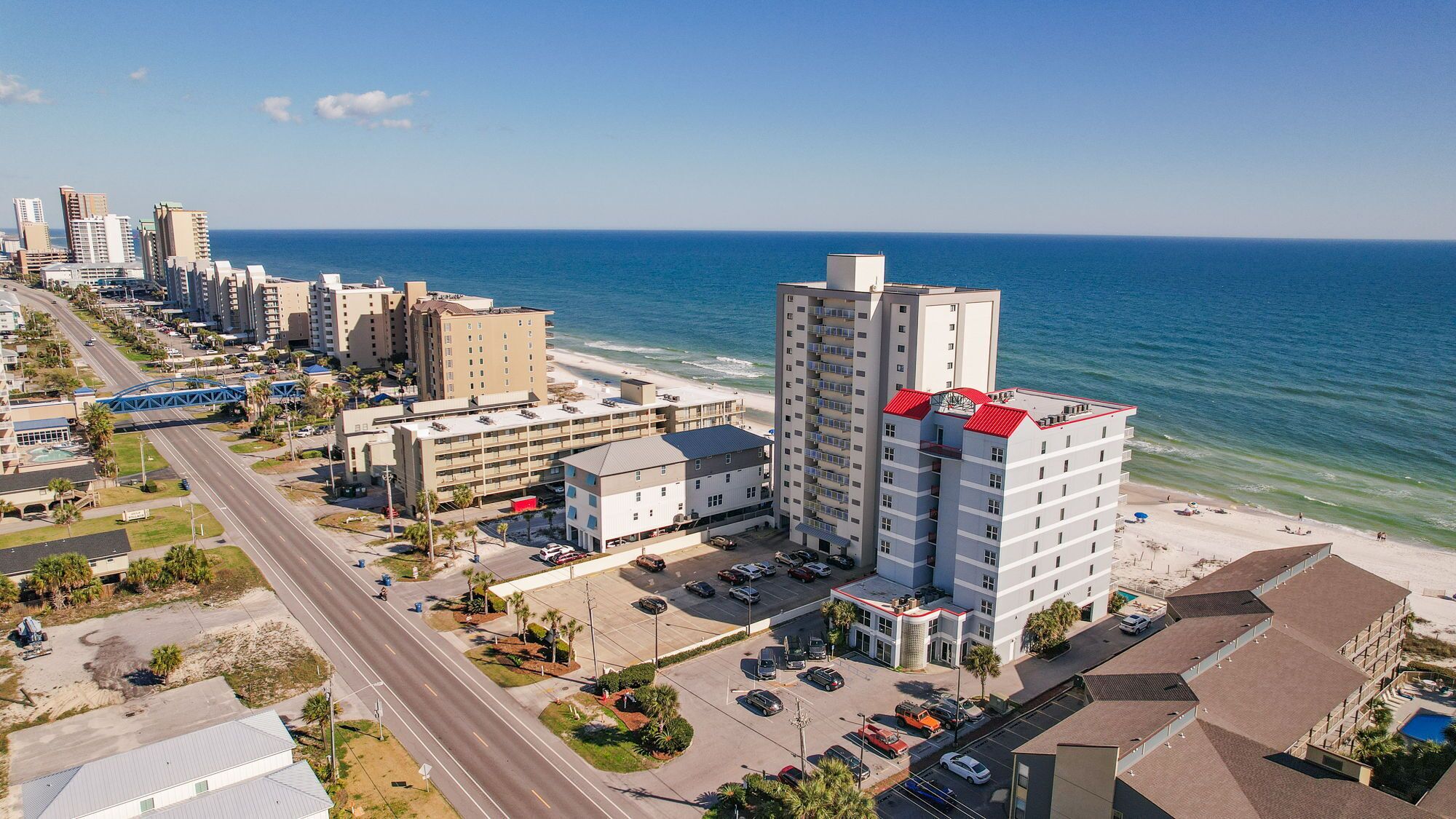Un hotel costero con varios pisos, estacionamiento y vista a la playa y al océano.