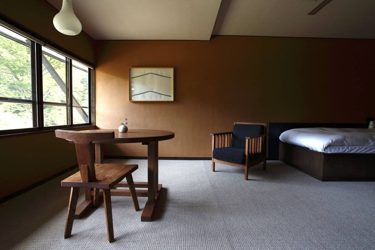 Un dormitorio moderno con una cama, una silla de madera, una mesita pequeña y un cuadro en la pared.