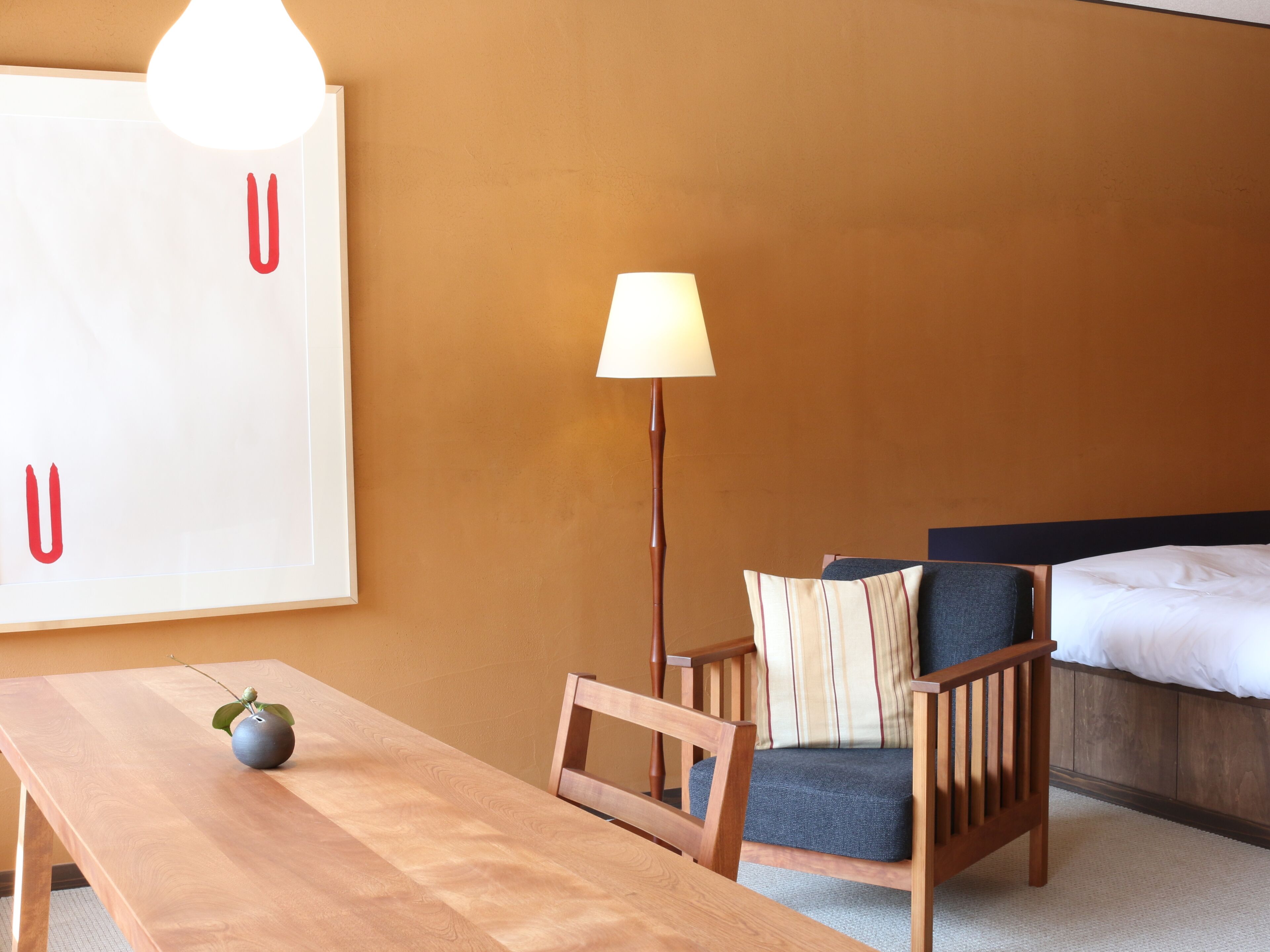 Ein Hotelzimmer mit Holztisch, Stuhl, Lampe, Bett und einer großen Wanddekoration.
