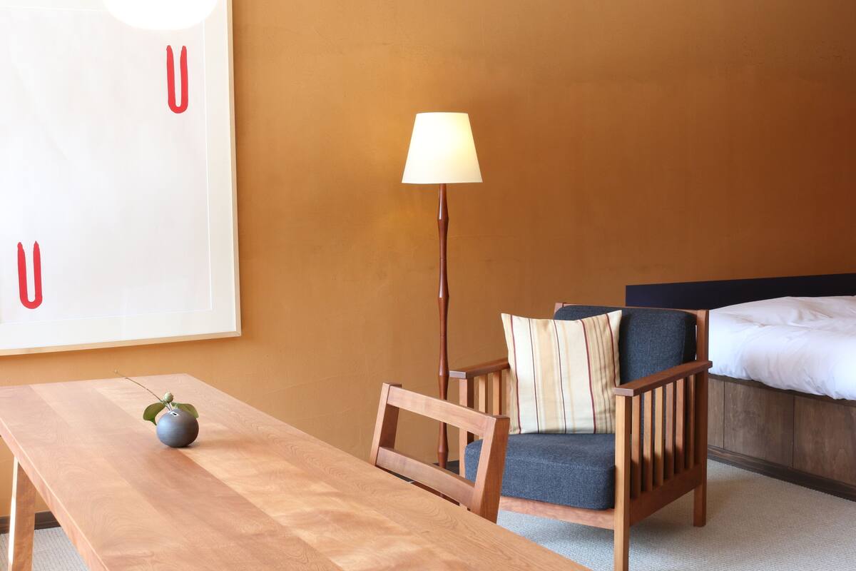Habitación de hotel con una mesa de madera, una silla, una lámpara, una cama y un adorno grande en la pared.