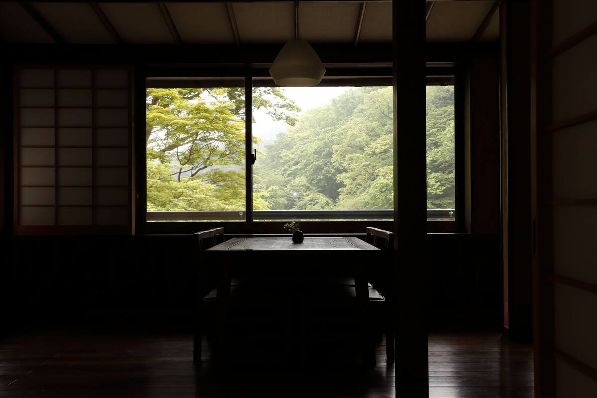 Una habitación japonesa tradicional con suelo de tatami, una mesa baja con un florero y un ventanal con vistas a un bosque.