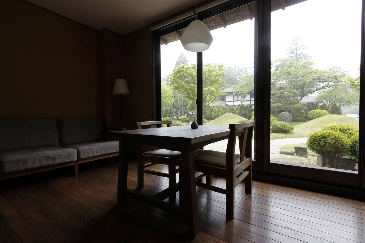 Una habitación con piso de madera, una mesa de comedor con sillas, un sofá y un ventanal con vistas a un jardín.