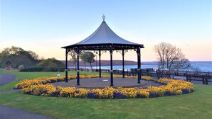 A gazebo with a curved roof and a central pole, surrounded by a circular flower bed with yellow flowers. - ❤️ Large Family Self Catering Holiday House-Filey (Filey)