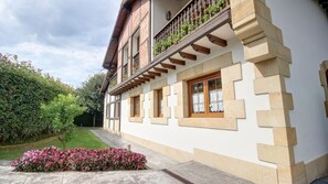 Ein zweistöckiges Gebäude mit Balkon, großen Fenstern und einem Garten mit rosa Blüten.