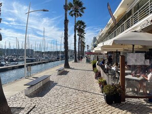 Enjoy waterfront views and outdoor seating areas with tables and chairs, shaded by umbrellas, amidst palm trees.
