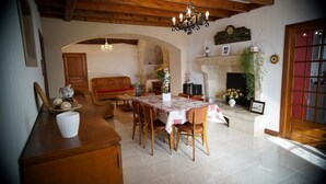 A dining area with a wooden table, chairs, and a chandelier. There is a fireplace with a mantle and a clock above it. - Cottage 4 people for lovers of the countryside (Poiseul-la-Ville-et-Laperrière)