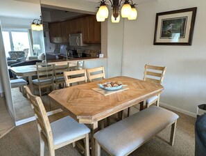 Un comedor con una mesa y sillas de madera, una pequeña isla con microondas y un cuadro en la pared.