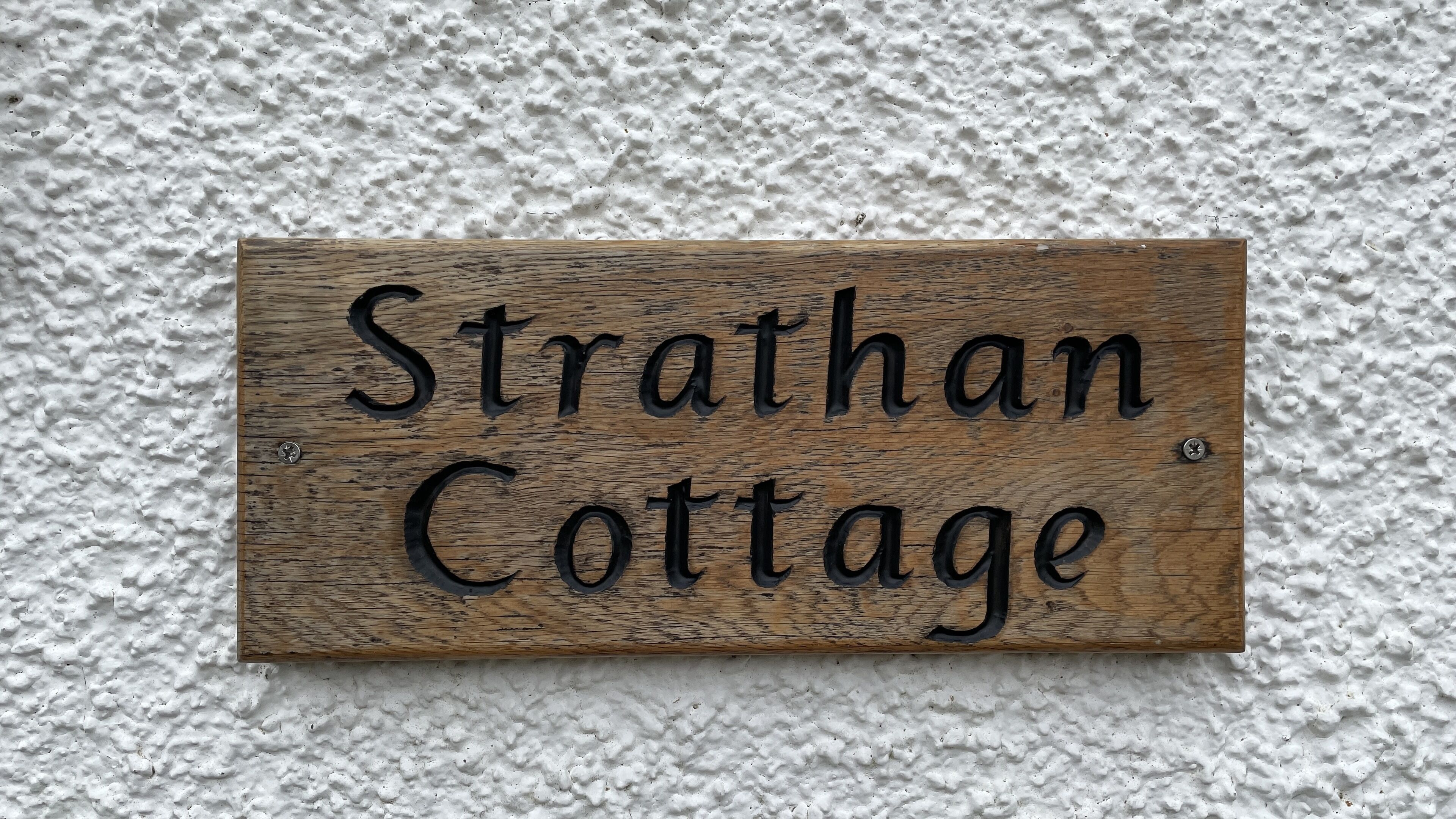 A wooden sign with the text "Strathan Cottage" against a textured white wall.