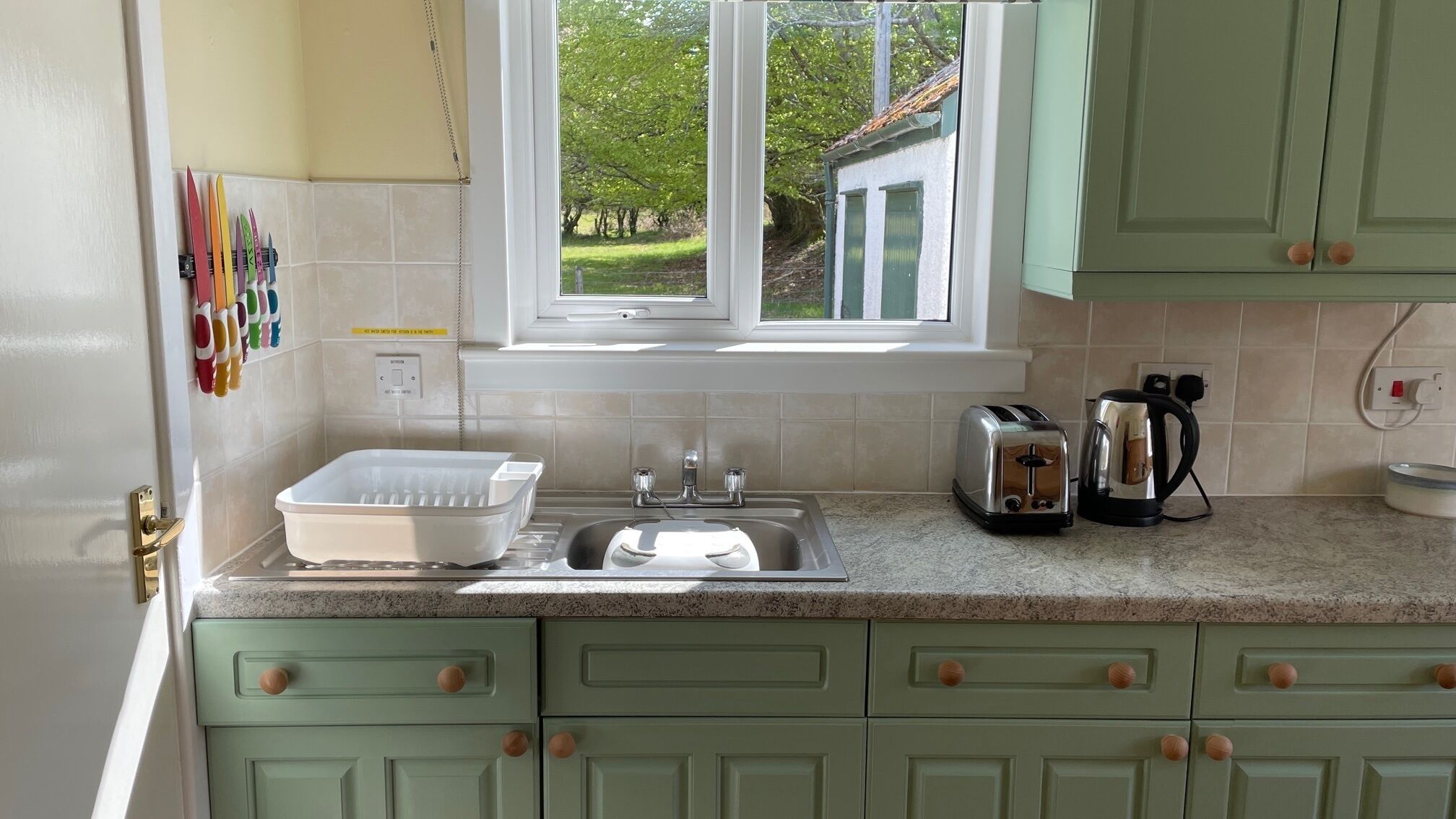 A kitchen with a window, a sink, a toaster, and a kettle.
