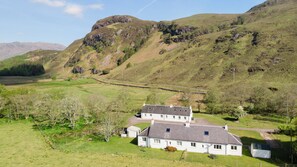 A rural house with a stone wall, surrounded by green fields and hills.
