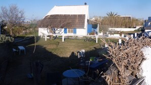 Ein weißes Haus mit Strohdach, einer kleinen Veranda und einem Gartenbereich mit Tischen und Stühlen.