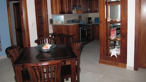 Un coin repas avec une table et des chaises en bois, une cuisine en arrière-plan et une étagère décorative ornée d’étoiles de mer.
