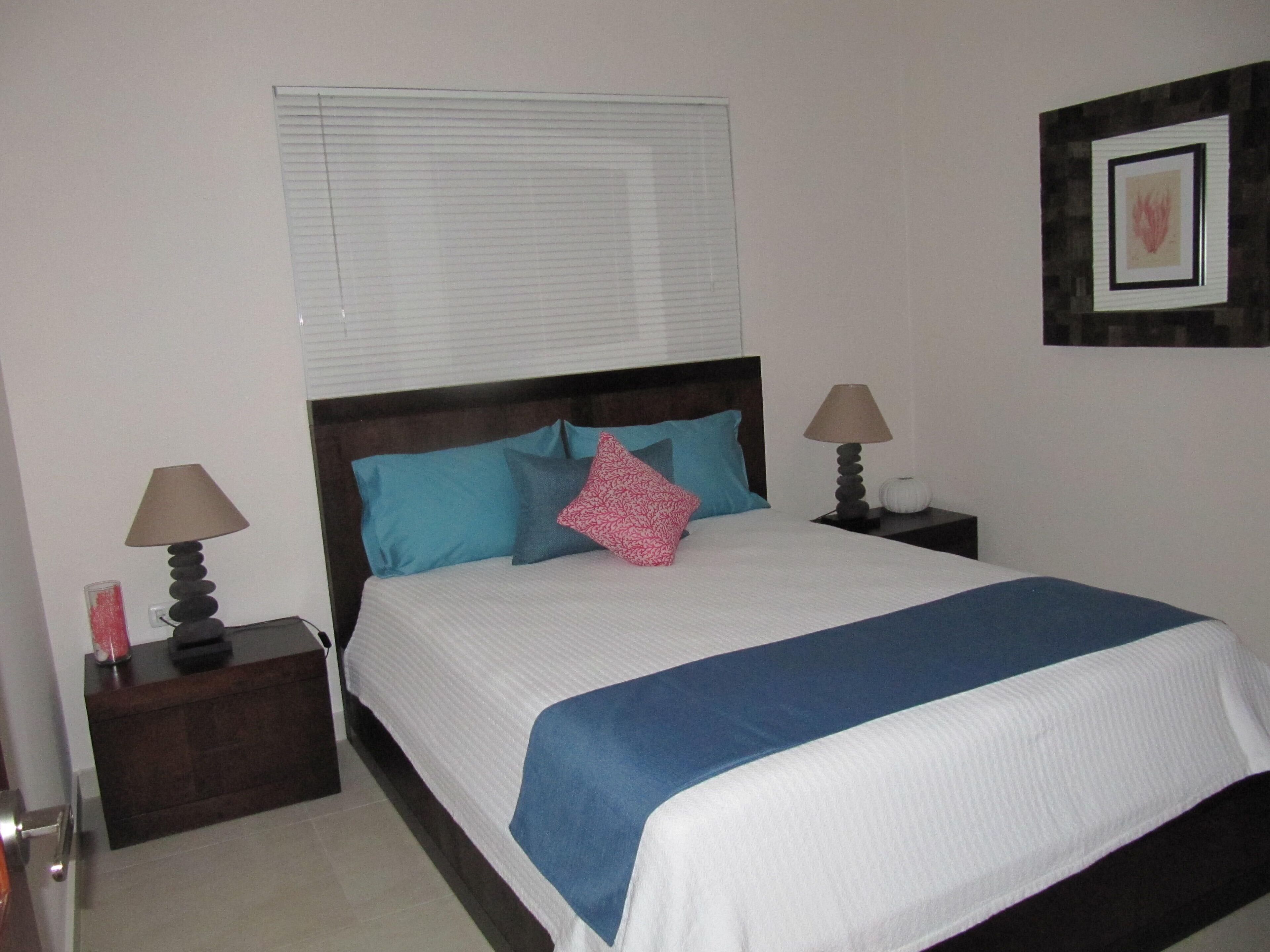 A neatly made bed with a blue and white bedspread, two bedside lamps, and a nightstand with a decorative item.