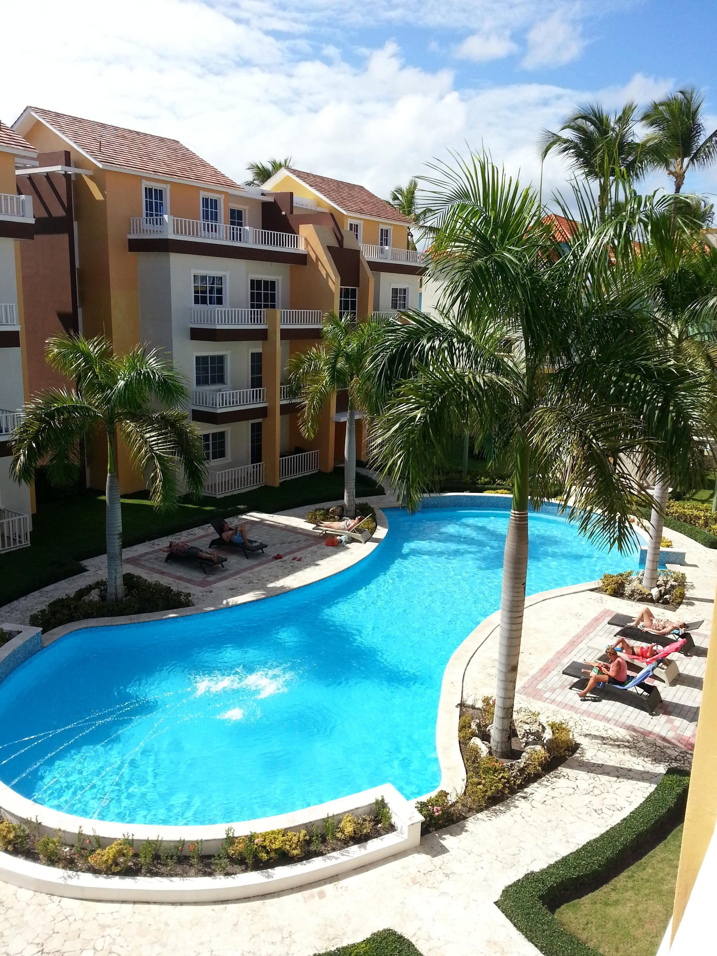 A resort with a swimming pool, palm trees, and a multi-story building with balconies.