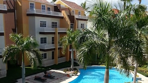 Un complexe hôtelier doté d’une piscine, de palmiers et d’un immeuble à plusieurs étages avec des balcons.