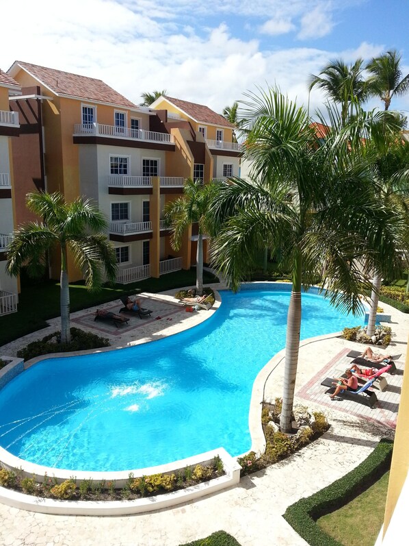 A resort with a swimming pool, palm trees, and a multi-story building with balconies.