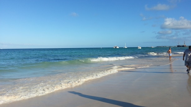 Une plage aux eaux calmes, un ciel dégagé et des bateaux à l’horizon.