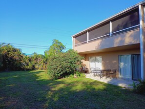Une maison à deux étages avec un balcon, une pelouse et une terrasse aménagée avec du mobilier d’extérieur.