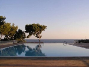 Piscina infinita con vista despejada al océano, rodeada de árboles y una valla.