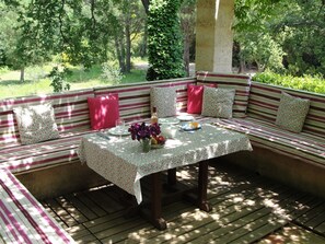 A covered outdoor seating area with a table, benches, and a view of a wooded area. - Idyllic St Tropez location with pool. Tranquil setting close to all the action. (Ramatuelle)