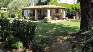 A two-story house with a patio area, surrounded by greenery and trees. - Idyllic St Tropez location with pool. Tranquil setting close to all the action. (Ramatuelle)