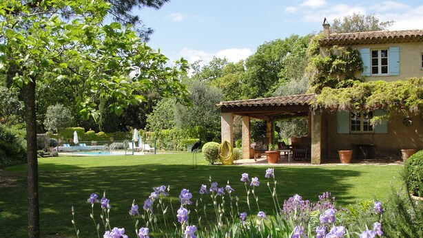 A house with a patio, surrounded by a well-maintained lawn and flowering plants. - Idyllic St Tropez location with pool. Tranquil setting close to all the action. (Ramatuelle)