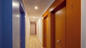 Un couloir doté d’un plancher en bois, de portes bleues et oranges, et d’un plafond pourvu d’un éclairage encastré.