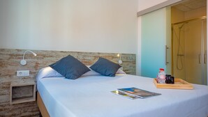 A neatly made bed with pillows, a bedside table with a magazine, a bottle, and a tray of toiletries. - Agi Gloria Rooms 106 Hostel for rent in Roses Girona. (Roses)