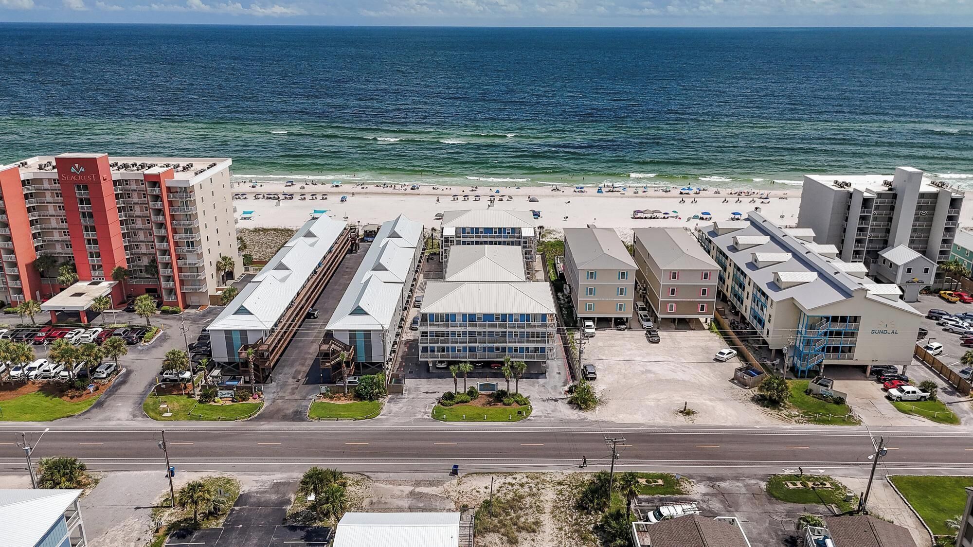 Ein Küstenhotel mit mehreren Gebäuden, einem Parkplatz und einem Strand im Hintergrund.
