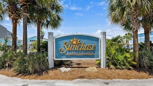 A sign for 'Sunchase Condominiums' with a sun emblem, surrounded by palm trees and a clear sky. - Recently refurnished condo directly on the beach! (Gulf Shores)
