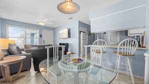 A modern living room with a glass dining table, white chairs, a sofa, and a ceiling fan. - Recently refurnished condo directly on the beach! (Gulf Shores)