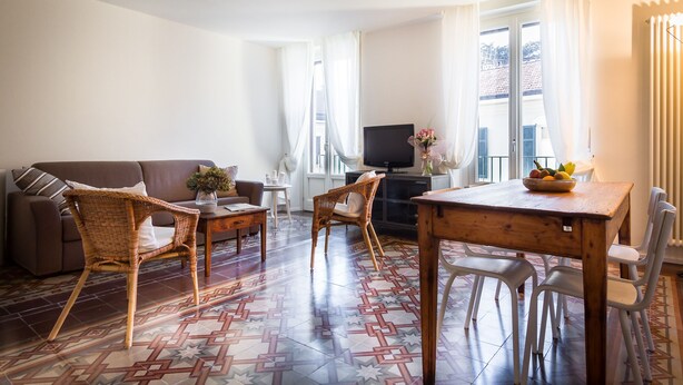 A living room with a sofa, two wicker chairs, a dining table with chairs, a TV, and a window with curtains. - REGINA  24 APARTAMENT (Cernobbio)