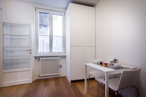 Ein kleiner, gut beleuchteter Raum mit einem für das Essen gedeckten weißen Tisch, einem Heizkörper und einem Fenster mit Vorhängen.