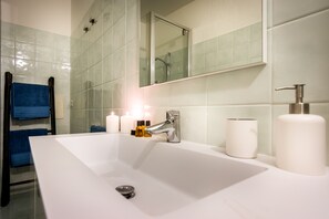 Ein Badezimmer mit einem großen weißen Waschbecken, einem Spiegel und einer Dusche.