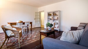 A living room with a sofa, a wicker chair, a dining table with chairs, and a bookshelf. - REGINA  24 APARTAMENT (Cernobbio)