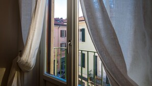 A window with curtains partially drawn, revealing a view of buildings with balconies and a street. - REGINA  24 APARTAMENT (Cernobbio)