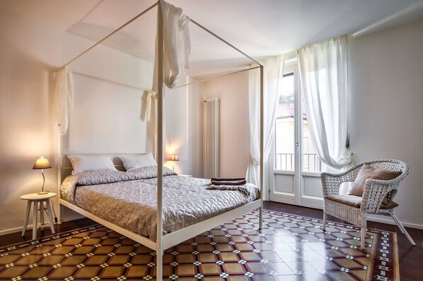 Ein Himmelbett mit weißem Baldachin, ein Korbsessel und ein gemustertes Teppich.