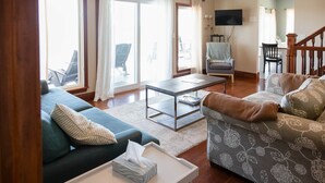 A living room with a sofa, armchair, coffee table, and a television mounted on the wall.