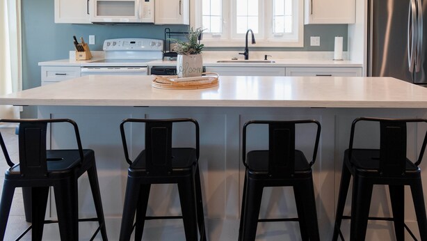 A kitchen with a large island, black bar stools, a microwave, and a stainless steel refrigerator.
