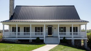 A two-story house with a front porch, a stone chimney, and a metal roof.