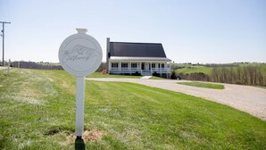 A sign with 'The Gathering' text, a house with a porch, and a grassy field.