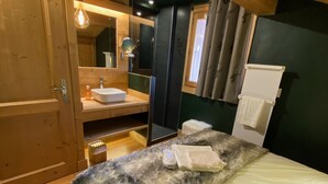 A bedroom with a wooden ceiling, a bed with a white mattress, a fluffy blanket, a wooden nightstand, a mirror, a sink, and a window with curtains. - Chalet Individual warm  (Megève)