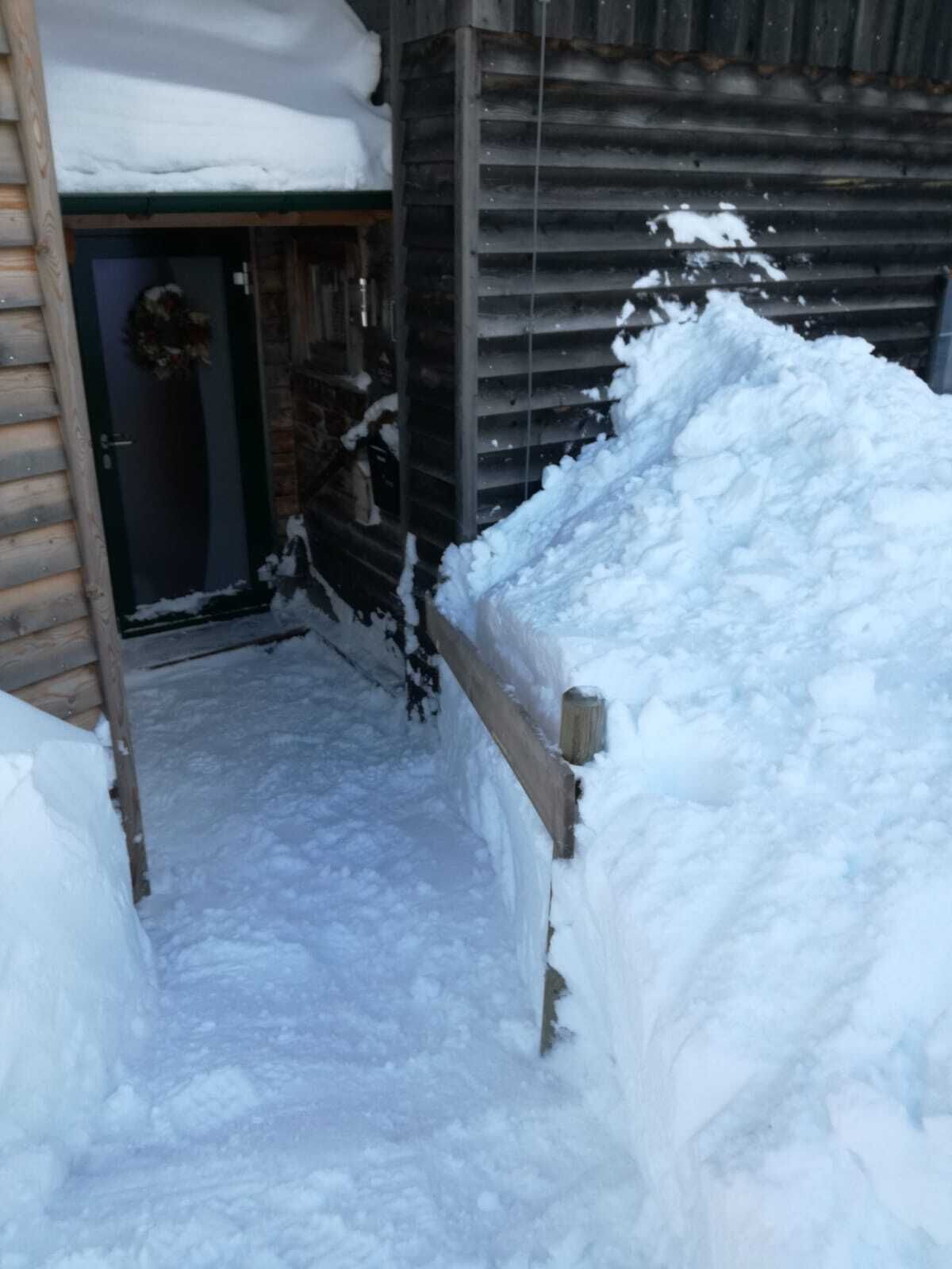 Ett snötäckt utomhusområde med ett trästaket och en grind av metall.